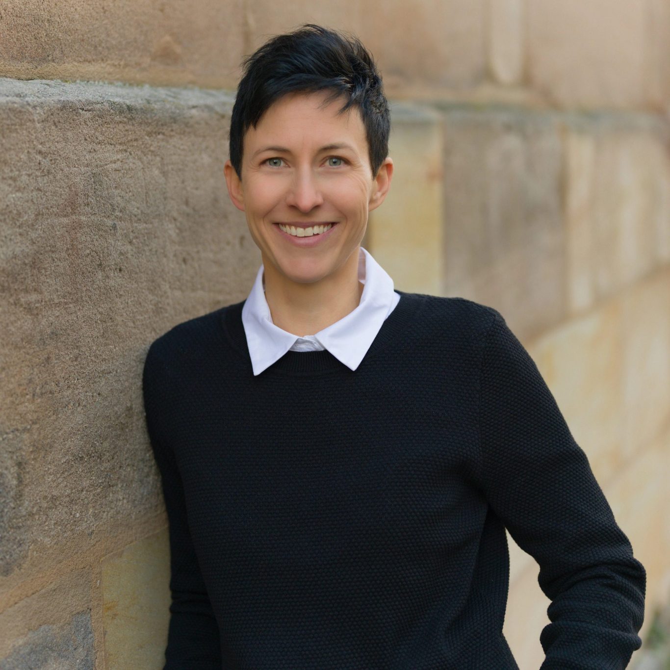 Ganzheitliches Coaching und Personal Training in Fürth Jennifer Meierhöfer, Life Coach und Personal Trainerin in Fürth, lehnt entspannt an einer Wand und lächelt in die Kamera.